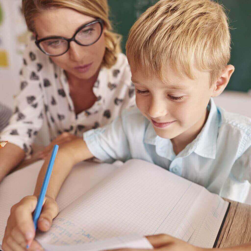 Imagem com uma mulher usando óculos e um menino loiro escrevendo em um caderno